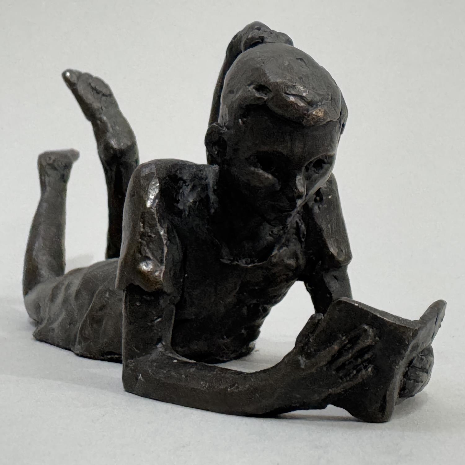 A bronze figure of a young girl reclining reading a book by Jonathan Sanders, Nelson and Forbes