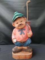 CARVED TEAK FIGURE OF A GOLFER with his golf bag over his shoulder and carrying a golf ball, with