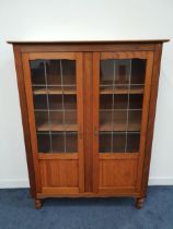 OAK BOOKCASE the rectangular top above a pair of three quarter leaded glass doors with panels below,