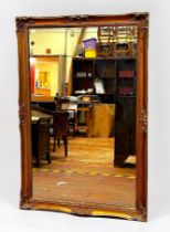 A large modern gilt framed rectangular mirror, with ornate scrolled and foliate decorated frame,