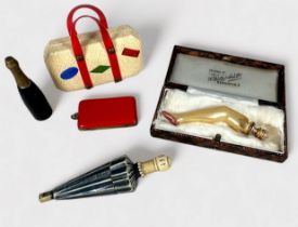 Five Novelty Needle Cases, comprising a suitcase, red purse, champagne bottle, glass leg with gold