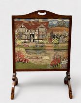 A glazed tapestry fire screen, depicting a a floral garden with figure stood in the doorway of a