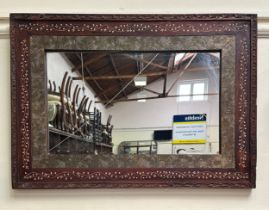 A hardwood retangular framed mirror, the frame with carved and painted decoration and swirl-embossed
