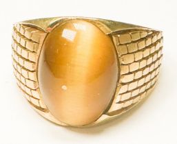 A yellow gold (tests as 18ct) gents dress ring, bezel-set with oval-shaped Tigers Eye stone, with