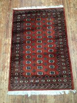 A hand-knotted Caucasian fringed wool rug with central field of stylized guls to a rouge ground