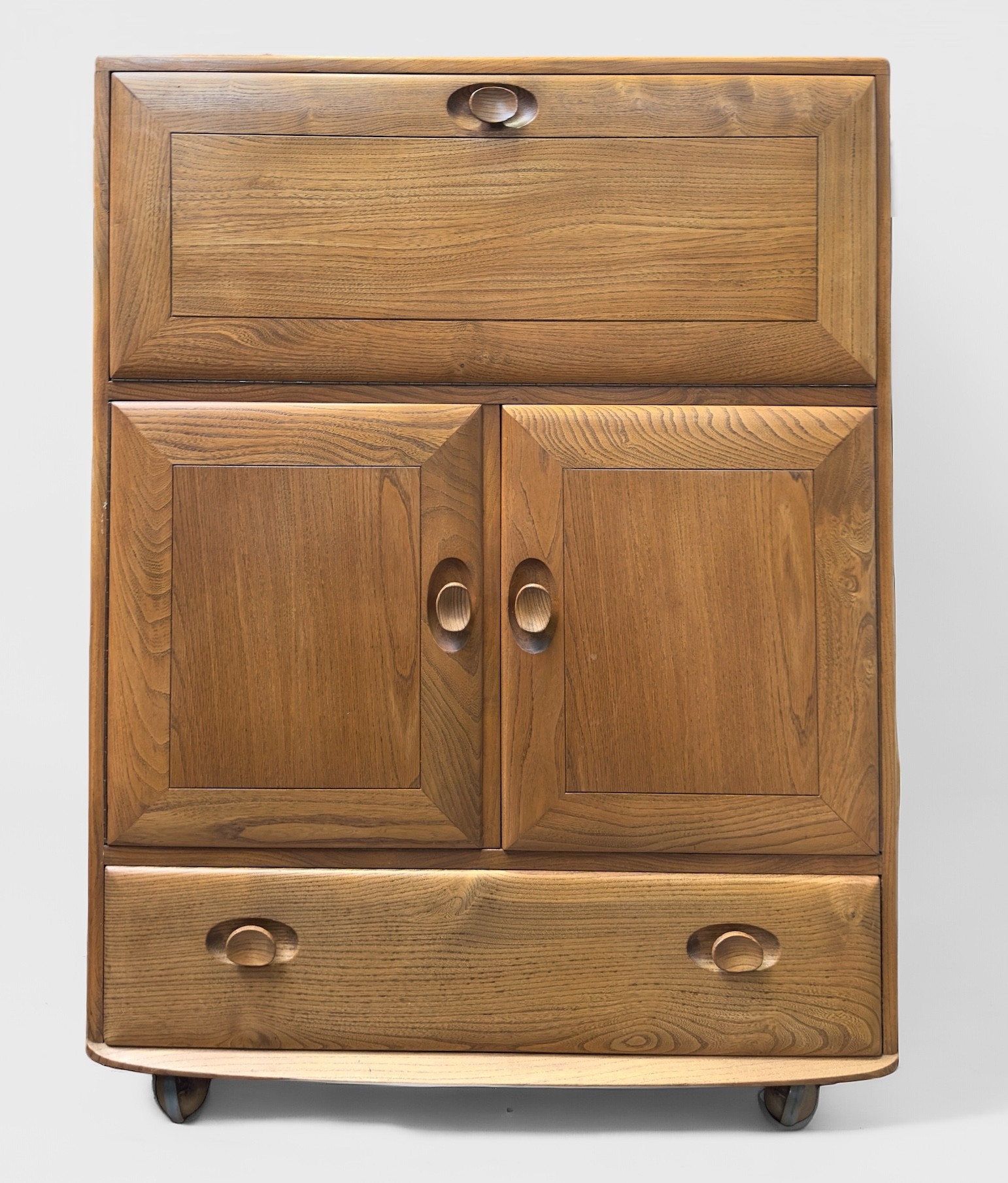 An Ercol blonde elm Windsor drinks cabinet, model 469, the fall-front enclosing compartmented