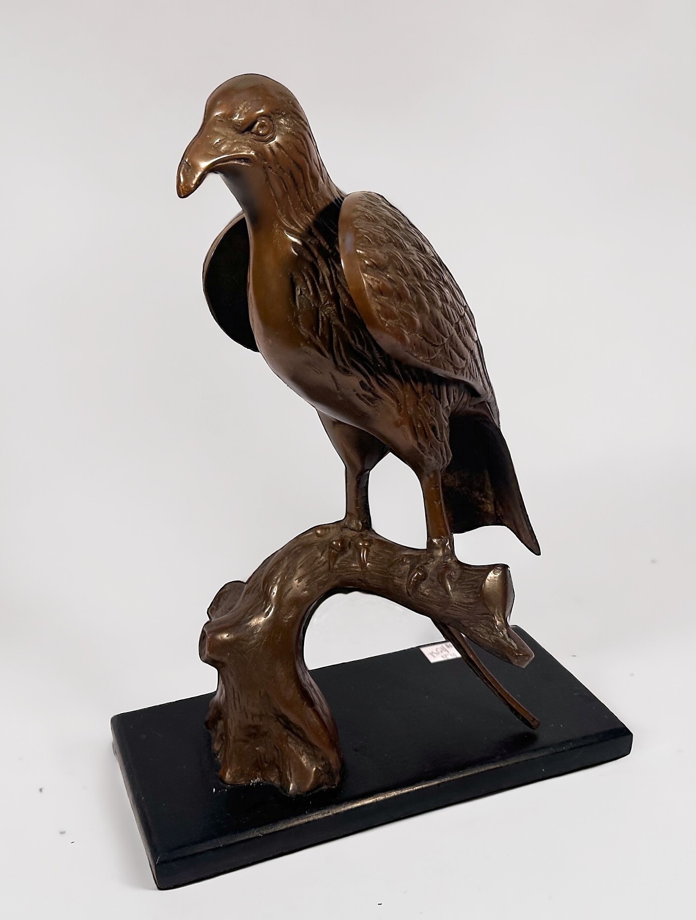 A copper alloy sculpture of an eagle perched on a branch, raised on stained wooden pedestal base,