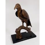 A copper alloy sculpture of an eagle perched on a branch, raised on stained wooden pedestal base,