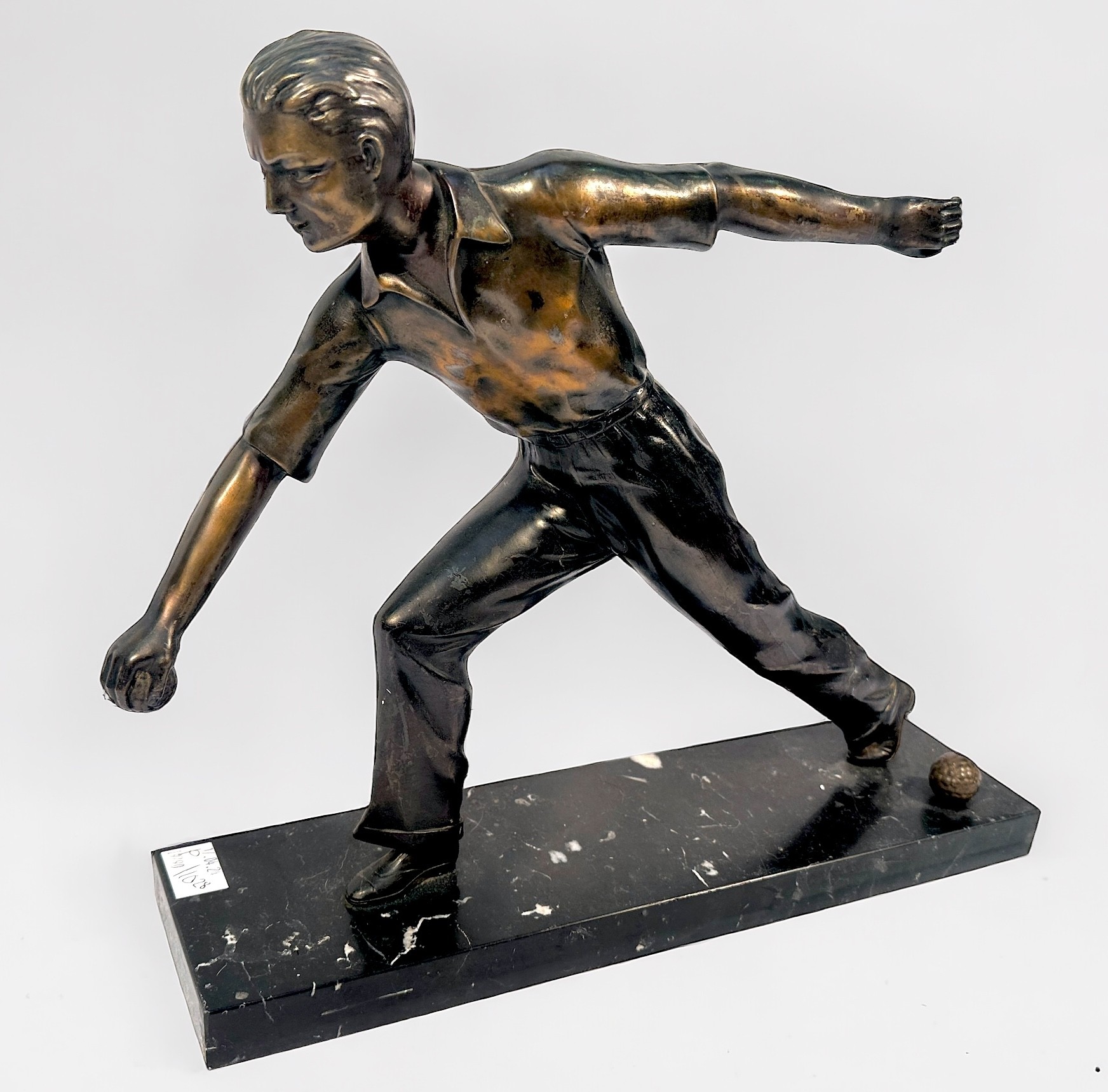 A bronzed metal sculpture of a man playing Pétanque, raised on marble base, 38cm long