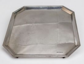 A silver salver, of square form with canted corners, raised on shaped rectangular bracket feet, ‘