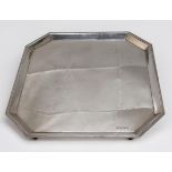A silver salver, of square form with canted corners, raised on shaped rectangular bracket feet, ‘