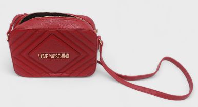 A red leather Love Moschino cross body bag, with gilt lettering to front and strap with gilt