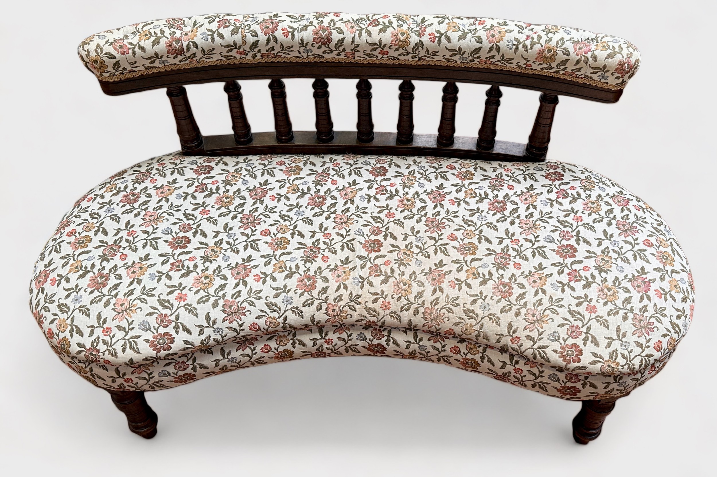 An Edwardian kidney-shaped parlour sofa, with bobbin spindle back and floral cream upholstered