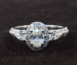A White Gold and Diamond Ring, centrally four-claw set with an oval faceted diamond with rbc