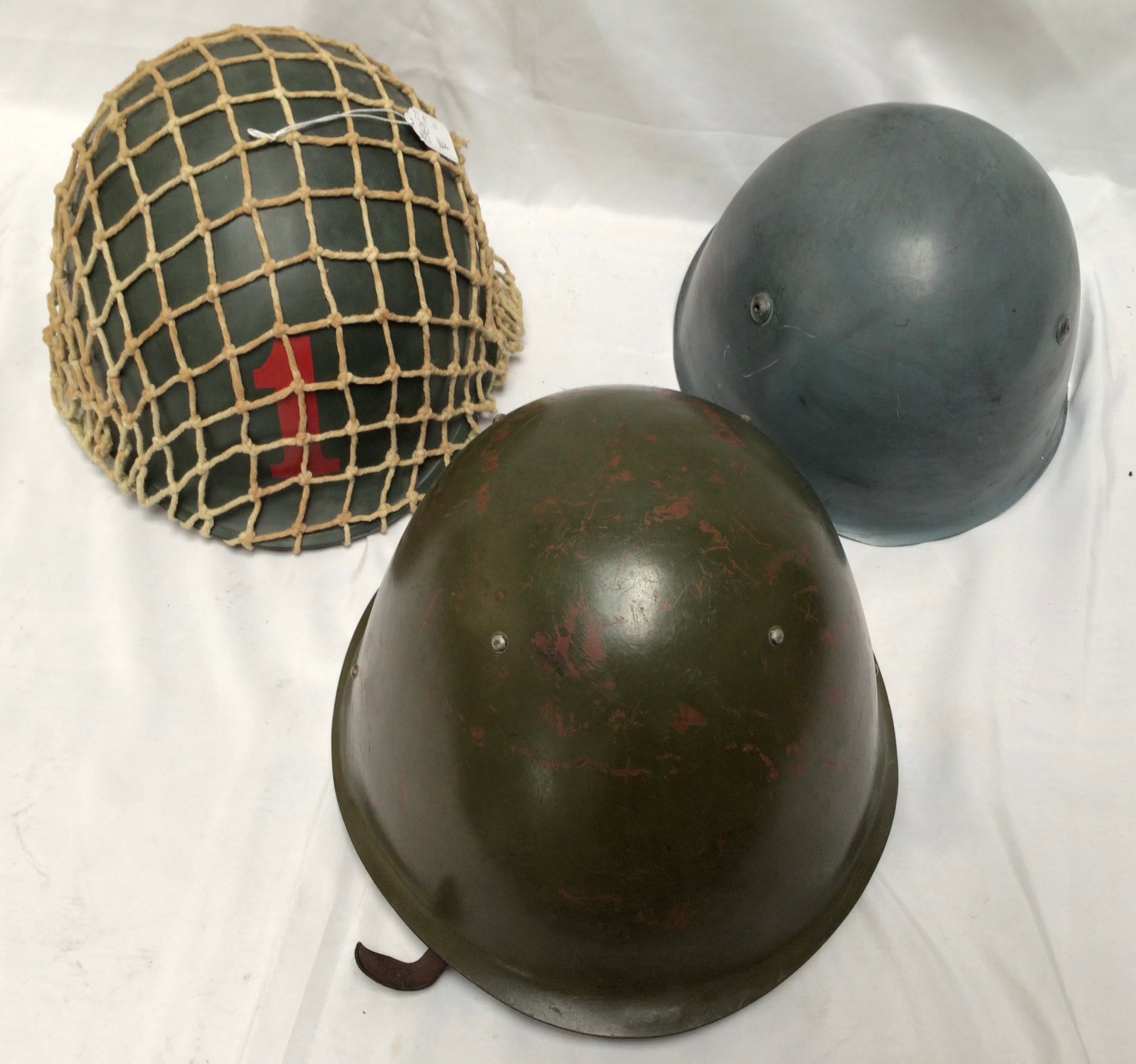 Three steel combat helmets, comprising an Italian M33 helmet, American U.S. M1 swivel bale helmet
