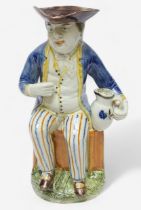 A Prattware Pottery ‘Sailor’ toby jug, c1790-1810, seated holding a jug, striped britches, blue coat