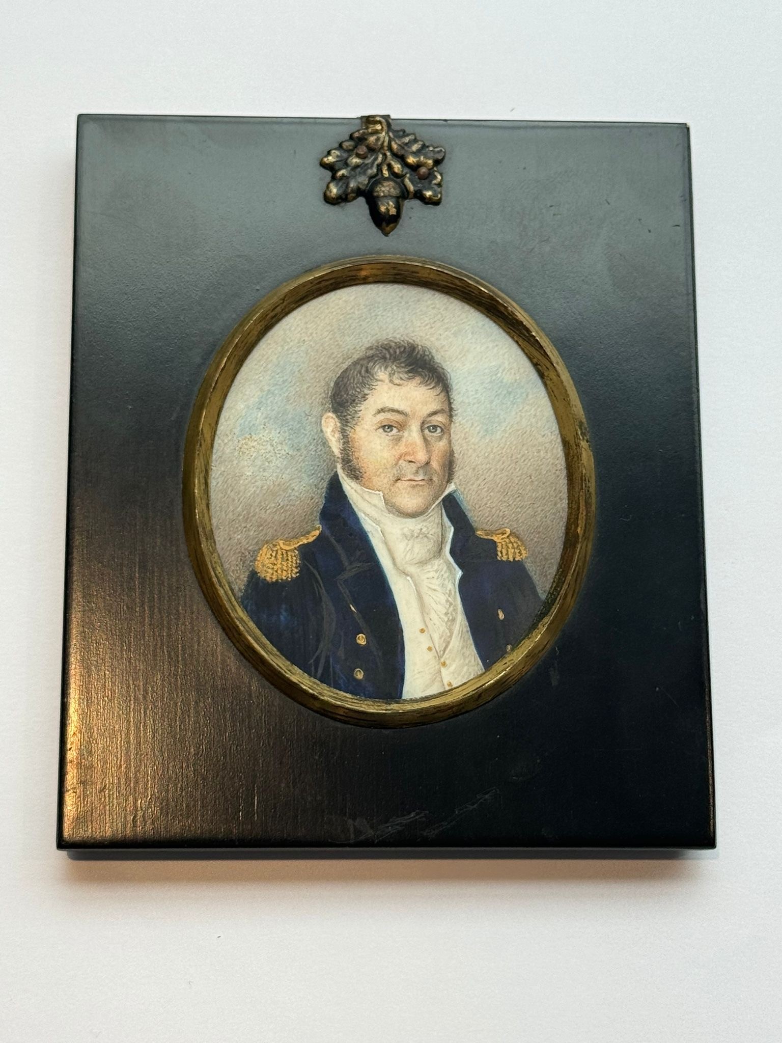 A 19th century oval portrait miniature of a middle-aged naval officer, with black hair and