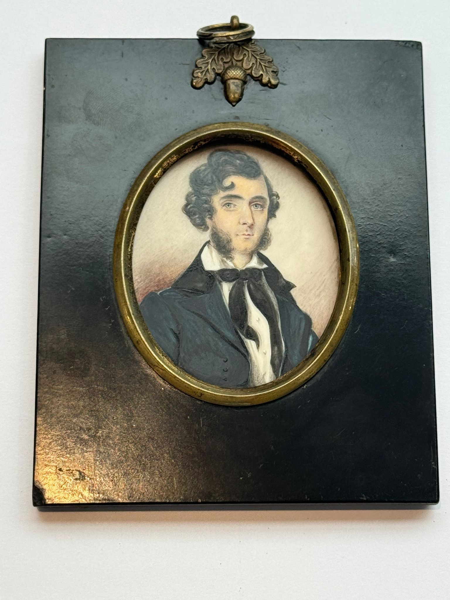 A 19th century oval portrait miniature of a young naval officer, with thick black wavy hair and ‘