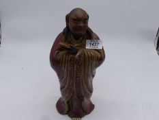 A Japanese red glazed stoneware figure of an Immortal holding a shoe, 11 1/4" tall.