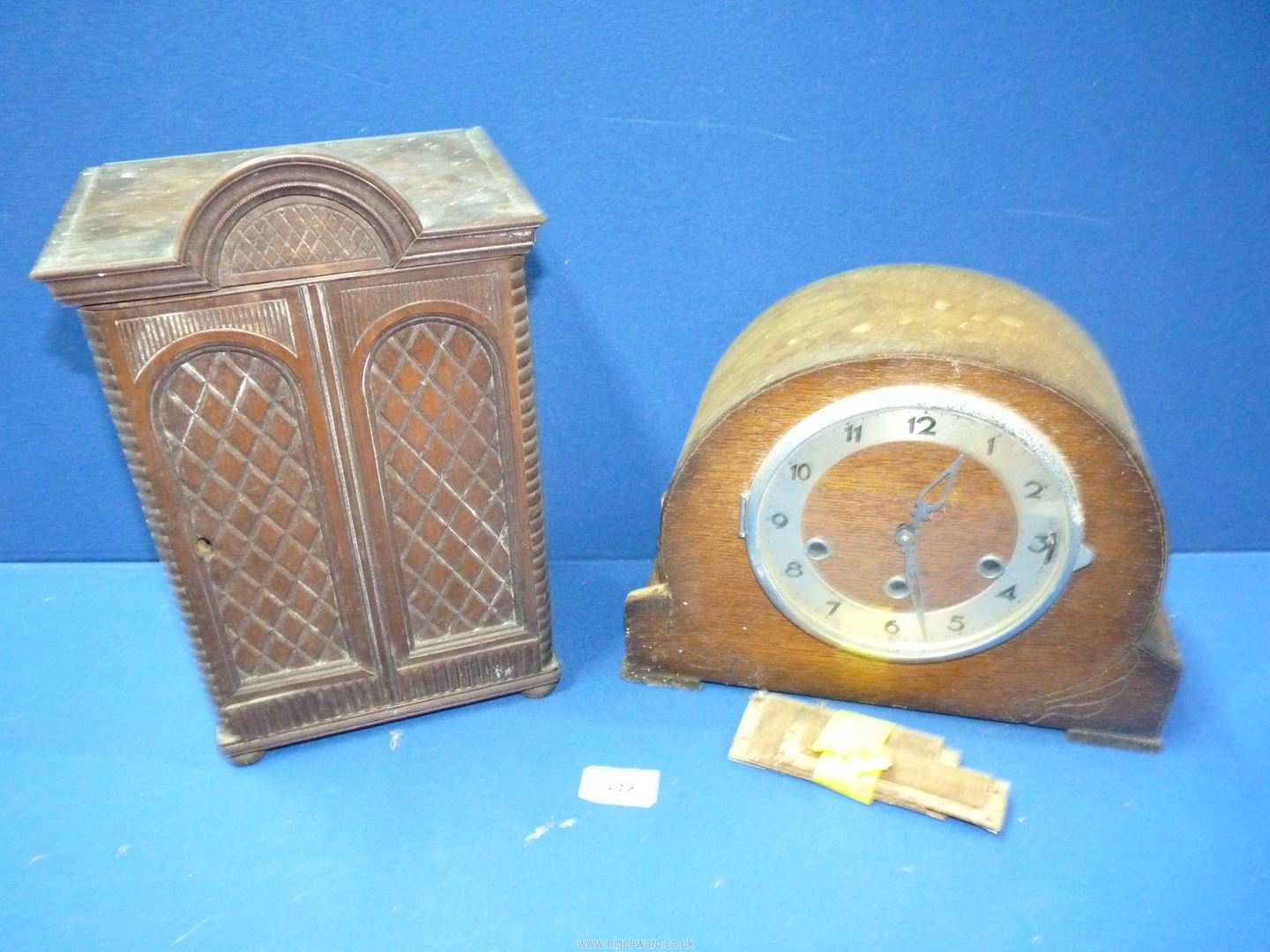 A dark wood cased mantle clock (damage to side) and a small darkwood cupboard with lattice design