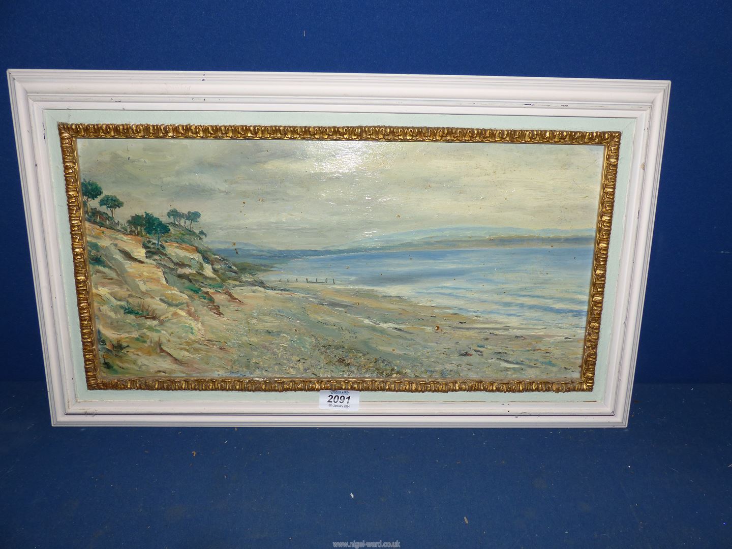 A framed Oil on board of a seascape with trees and rocky cliff to the foreground and hills in the