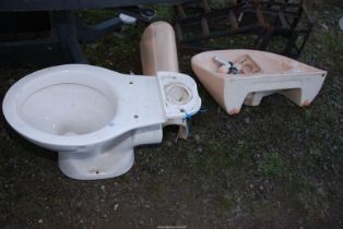 A Toilet system and a terracotta coloured Hand-basin with pedestal.