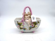 A porcelain flower encrusted basket with two cherubs embracing, 8" wide x 8 1/2" high.