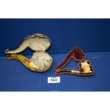 Two antique meerschaum Pipes, cased with amber stems, the larger one carved as a male lion's head,