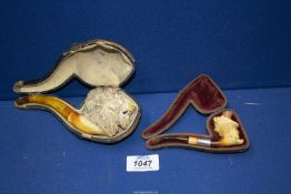 Two antique meerschaum Pipes, cased with amber stems, the larger one carved as a male lion's head,