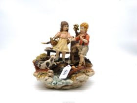 A Capo di Monte ornament of a girl and a boy on a bridge with a dog at their feet,