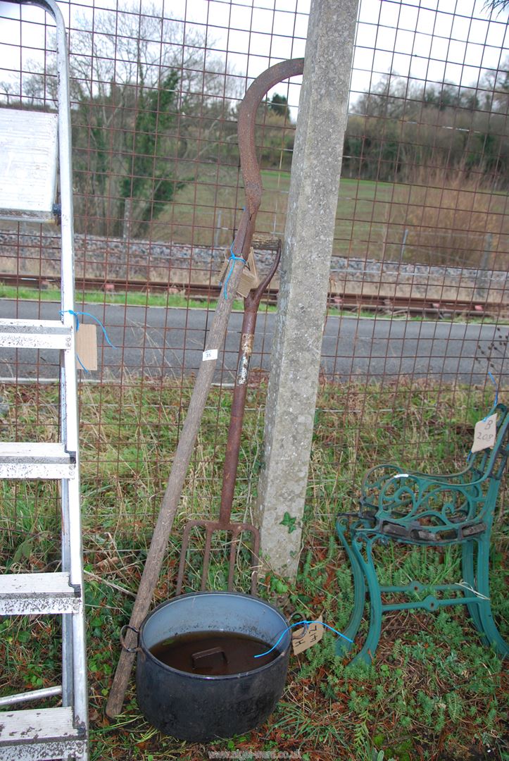 A cast iron oval range pot, hedge bill and a metal handled garden fork.