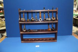 A 24 bay hardwood Pipe Rack with 12 briar and wooden pipes.