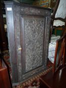 A wall hanging Oak Corner Cupboard having an intricately carved raised and fielded panelled door