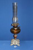 An oil lamp with ornate floral cast metal base, stone column and an amber glass reservoir,