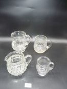 Four clear glass water and milk jugs - one with chip to rim.