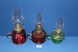 Two hand held Cranberry glass Oil lamps and one of green glass, all with chimneys.