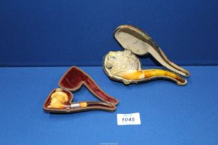 Two antique meerschaum Pipes, cased with amber stems, the larger one carved as a male lion's head,