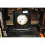A plain slate chiming Mantle Clock having Roman numerals on a white face and a clear glass back
