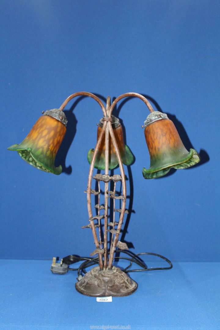 A three branch Lily table lamp having a cast metal floral base and green/orange shades,