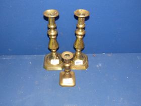A pair of brass candlesticks with pushers, plus one other.