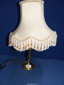 A brass candlestick converted to an electric table lamp, with tasselled and beaded shade.