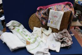 A wicker basket with a selection of linen including embroidered linen.