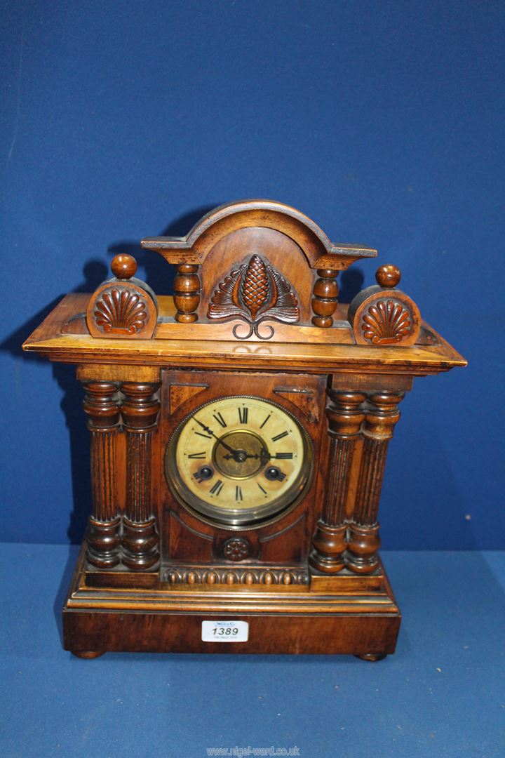 A Mantle clock with pine cone detail to the pediment and columns to either side of the clock face,