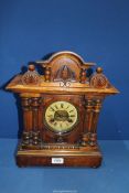 A Mantle clock with pine cone detail to the pediment and columns to either side of the clock face,