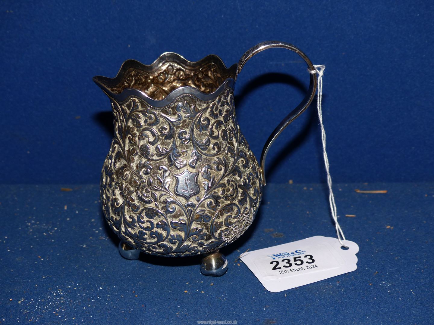 A white metal repousse Cream Jug on three ball feet with wavy rim,