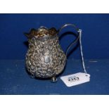 A white metal repousse Cream Jug on three ball feet with wavy rim,