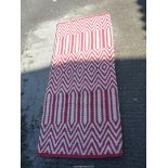 A red and white wool hearth rug, zig-zag and diamond patterns, 63" x 28", some stitching loose.