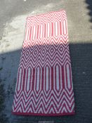A red and white wool hearth rug, zig-zag and diamond patterns, 63" x 28", some stitching loose.