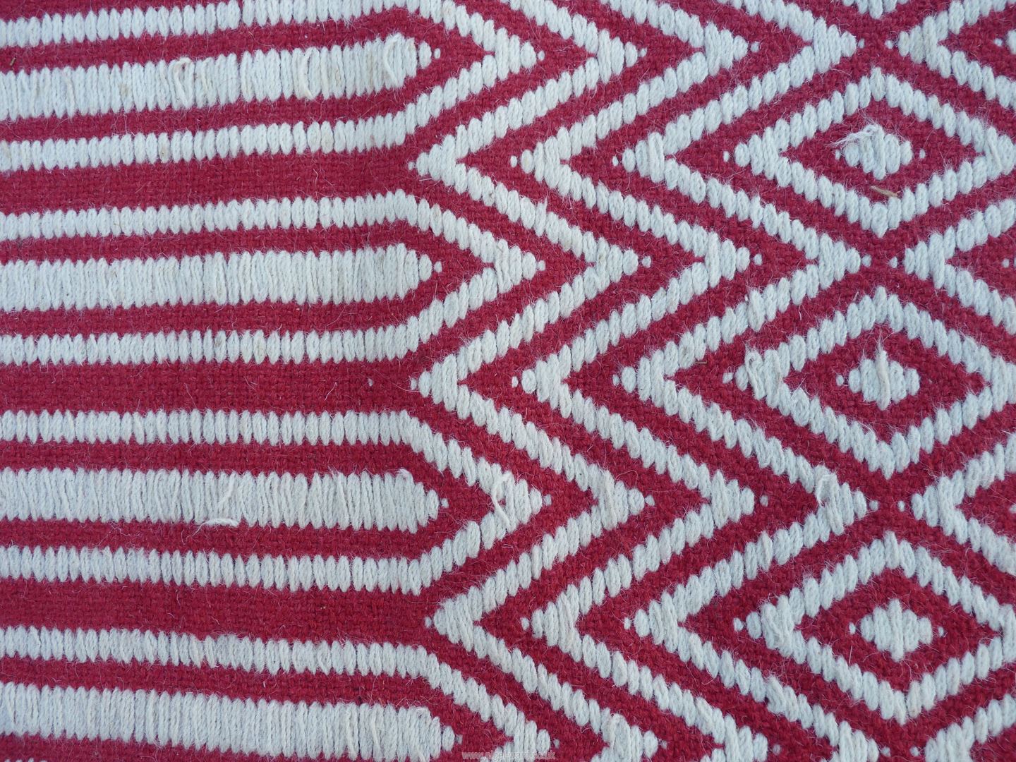 A red and white wool hearth rug, zig-zag and diamond patterns, 63" x 28", some stitching loose. - Image 2 of 3