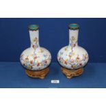 A pair of cloisonné bottle neck baluster vases decorated with blossom and butterflies on a wooden